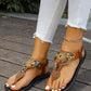Bohemian brown flat sandals adorned with vibrant multicolor beads and golden mandala charms, featuring a braided elastic ankle strap worn by a model with white jeans.