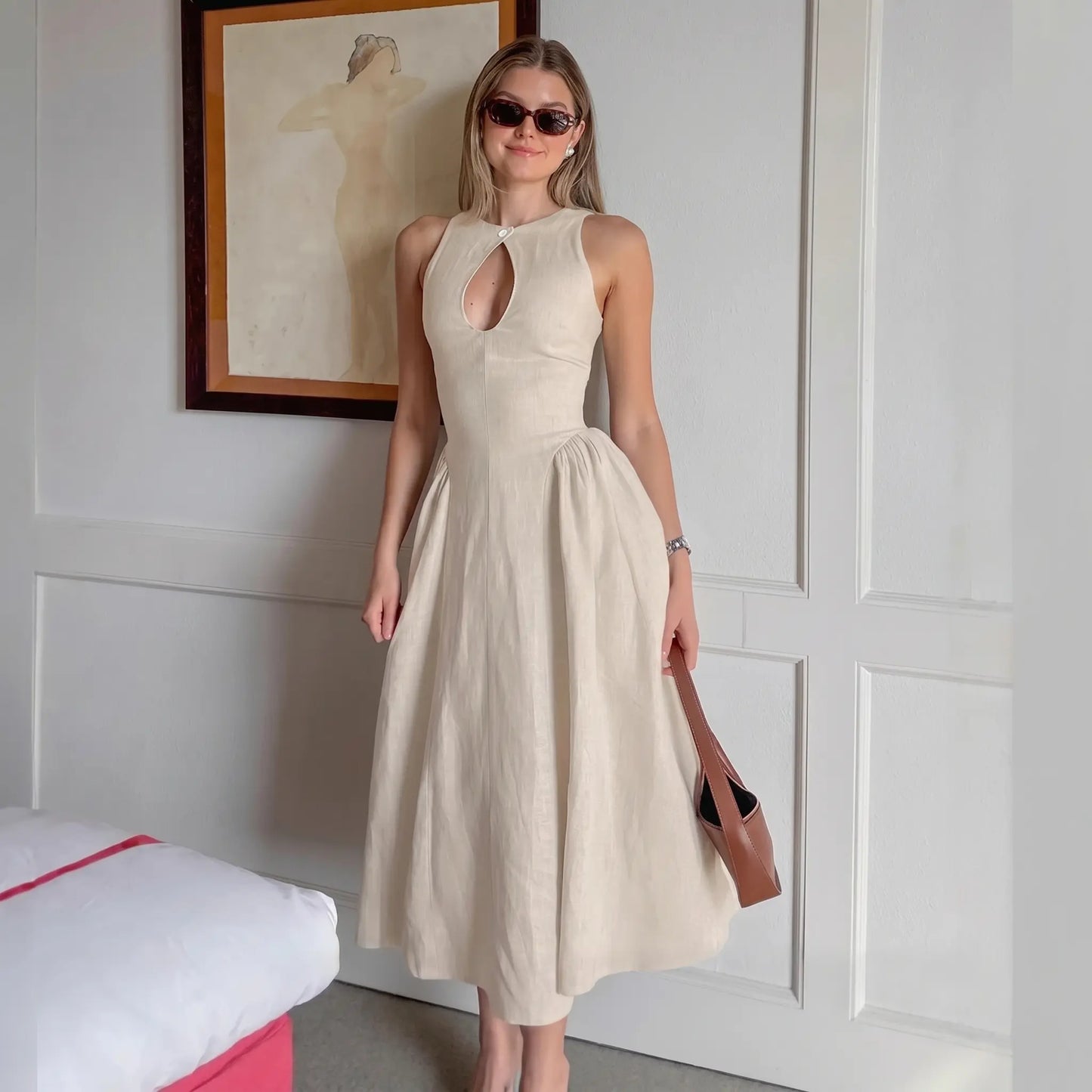 A woman models a sleeveless, light beige linen-blend midi dress with a keyhole neckline and a gathered A-line skirt, standing in a styled room setting.