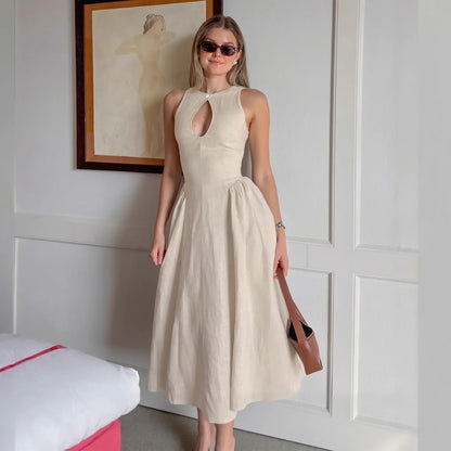 A woman models a sleeveless, light beige linen-blend midi dress with a keyhole neckline and a gathered A-line skirt, standing in a styled room setting.