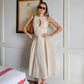 A woman models a sleeveless, natural beige linen-blend midi dress with a keyhole neckline and gathered A-line skirt, styled with sunglasses and a handbag.