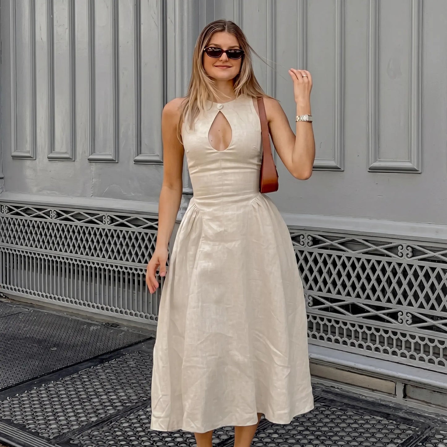 Woman wearing a Kalira sleeveless linen-blend midi dress in natural beige, featuring a keyhole neckline with a button and a gathered A-line skirt, styled for an elegant bohemian look.