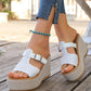 Woman wearing white woven platform espadrille sandals with T-strap and antique gold buckle, styled with flared denim jeans and a turquoise anklet.
