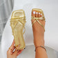 Close-up view of chic metallic gold square-toe flat sandals with delicate knotted straps, shown on a foot and held by a hand, showcasing the slip-on design and shimmering finish.
