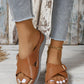 Kalyx women's brown faux leather wedge sandals featuring elegant criss-cross straps with micro-perforations and a gold-tone adjustable buckle, styled with denim jeans on a wooden floor.