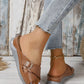 Kalyx women's brown faux leather wedge sandals with elegant criss-cross straps, gold-tone buckle, and micro-perforations, shown worn with denim jeans.