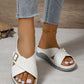 White women's Kalyx comfort wedge sandals featuring elegant criss-cross straps with micro-perforations and an adjustable gold-tone buckle, worn with light blue jeans.