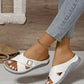 Elegant white Kalyx comfort wedge sandals with criss-cross straps, micro-perforations, and a gold buckle, shown on a woman's feet paired with denim.