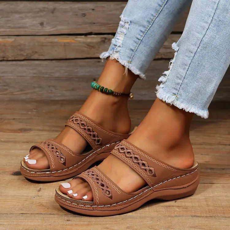 Kazari women's brown PU leather slide sandals with intricate geometric embroidered straps and a subtle wedge sole, worn with distressed jeans and an anklet.