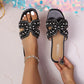 Elegant black Kezia flat sandals adorned with lustrous pearls and sparkling rhinestones, worn on a foot with white toenails and a delicate anklet.