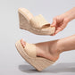 Natural khaki beige woven espadrille wedge sandals, one held by a hand and one worn on a foot, showcasing the braided raffia strap and jute rope heel.