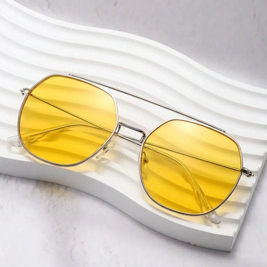 Khori aviator sunglasses with a silver metal double bridge frame and bright golden yellow gradient lenses, displayed on a white sculpted surface.