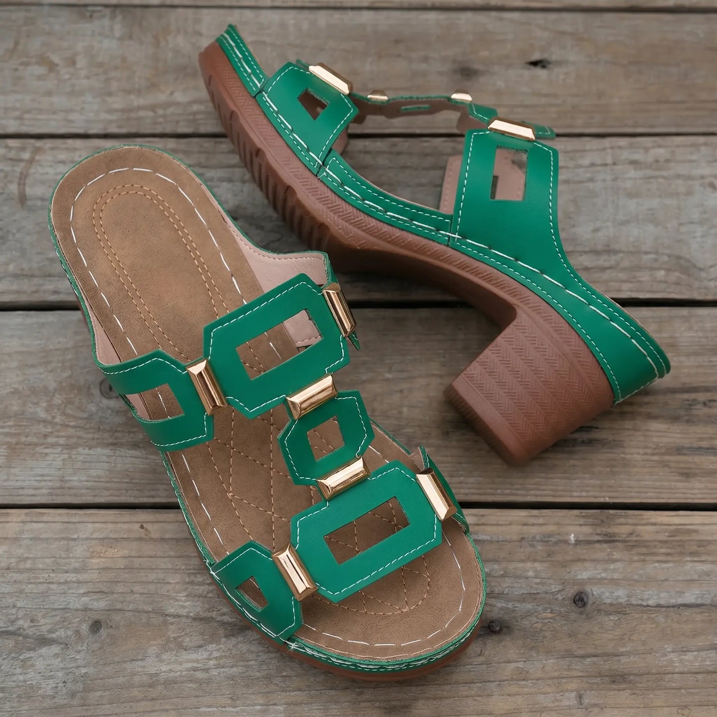 Emerald green heeled slide sandals for women, featuring a wide strap with geometric gold-tone hardware, white contrast stitching, a 3cm platform, and a 7cm chunky block heel on a wooden plank background.