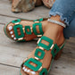 Close-up of green Khoros heeled platform slide sandals with gold geometric hardware, worn by a model with white-painted toenails and a diamond anklet, styled with distressed denim jeans on a wooden plank surface.