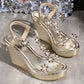 A pair of Khosha sparkling gold wedge sandals adorned with clear PVC straps featuring crystal floral embellishments and a textured metallic wedge heel.