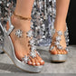 Khosha silver sparkling wedge sandals featuring transparent crystal floral straps and a textured metallic wedge heel, worn on feet with a gold ankle chain.