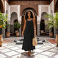 Elegant black Khozun Bohemian Open-Back Maxi Dress with spaghetti straps and gathered neckline, styled on a woman walking in an ornate courtyard.