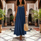 Woman models a Khozun navy blue bohemian oversized maxi dress with delicate spaghetti straps and a gathered scoop neckline, walking through an elegant Moroccan courtyard.