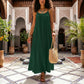 Khozun Deep Emerald Bohemian Open-Back Maxi Dress with delicate spaghetti straps and gathered scoop neck, featuring a voluminous tent silhouette, worn by a model walking in a Moroccan courtyard with a woven bag and sandals.