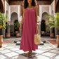 Khozun Deep Rose Bohemian maxi dress with thin spaghetti straps and a gathered scoop neckline, worn by a model walking in an ornate courtyard.