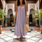 Model wearing a Lavender Whisper Khozun bohemian maxi dress with spaghetti straps and a gathered scoop neckline, walking through an ornate tiled courtyard.