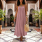 Khozun Lotus Pink bohemian maxi dress with thin spaghetti straps and gathered scoop neckline, worn by a model walking in an ornate courtyard.