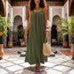 Model walking in an Olive Drab Khozun Bohemian Open-Back Maxi Dress with spaghetti straps and gathered scoop neckline, showcasing its voluminous silhouette in a Moroccan courtyard.