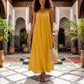Elegant woman in a Khozun Sunlit Yellow Bohemian Maxi Dress with delicate spaghetti straps and a gathered neckline, walking in a beautiful tiled courtyard.