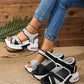 Women's black and grey woven textile platform sandals with a bow detail and hook-and-loop ankle strap, shown on a model's foot with a textured straw and wood background.