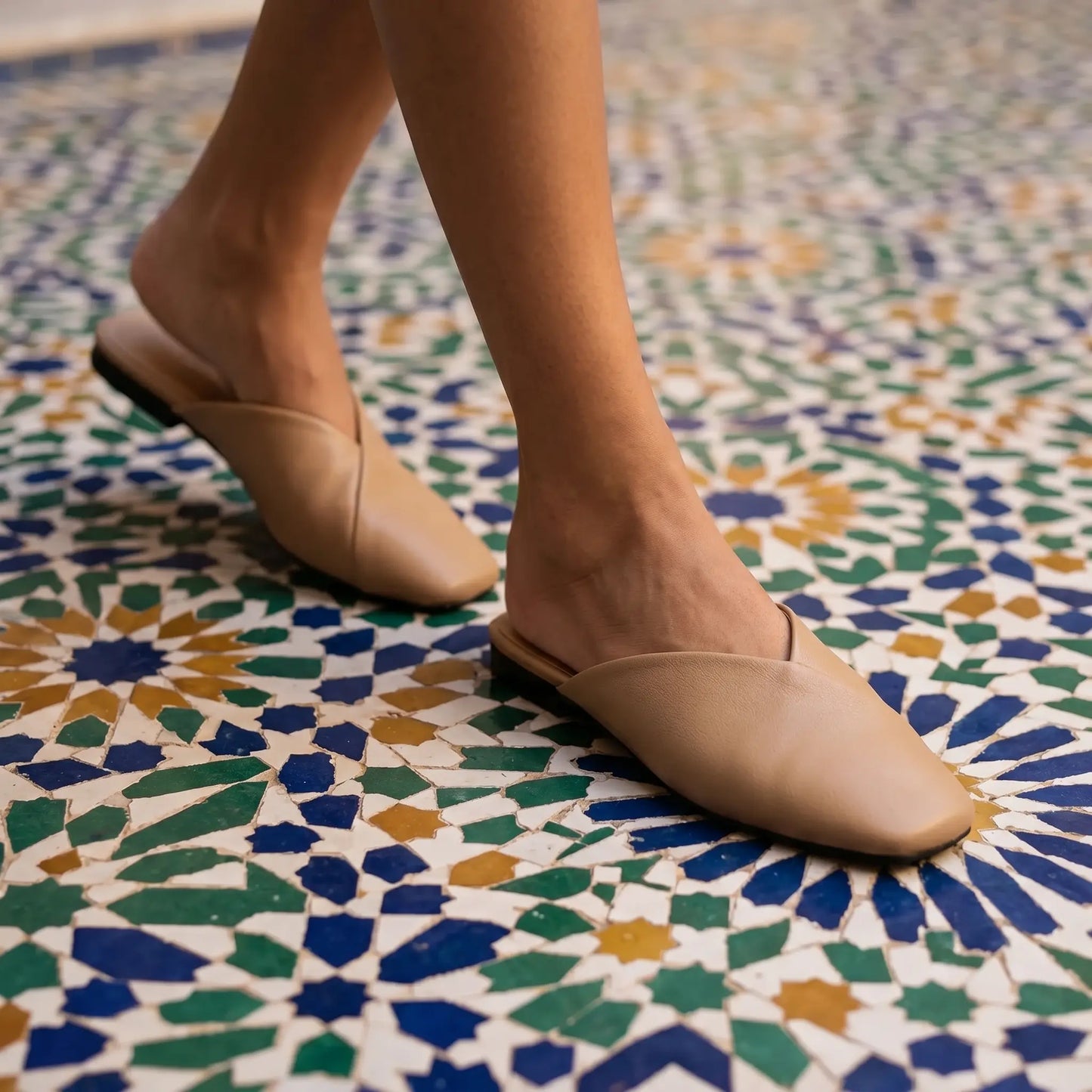 Khyren Alabaster Beige vegan leather V-vamp mule flats with square toes, worn by a model walking on a vibrant mosaic tiled floor.