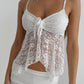Kirae white floral lace camisole with adjustable spaghetti straps and a tie-front detail, showcasing its cropped silhouette and scalloped hem.
