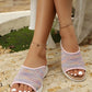 Women's Kithra pastel rainbow knit slide sandals with a contoured tan footbed and white EVA sole, shown on feet with white nail polish in an outdoor setting.