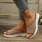 A woman's feet wearing tan, breathable knit Kithra comfort slide sandals with a contoured footbed, styled with distressed jeans and a gold anklet, resting on a wooden floor.
