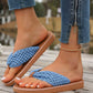 Woman wearing blue woven strap Koreli bohemian flat sandals with a tan sole, paired with denim jeans and an anklet, on a wooden deck.