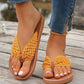 Koreli mustard yellow woven strap flat thong sandals worn by a woman with white toenails, paired with blue jeans and an anklet on a wooden deck.