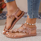 Close-up of pink bohemian flat thong sandals with delicate floral appliques and clear rhinestone embellishments, worn on feet with blue denim jeans and a white beaded anklet.