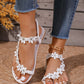 White Korynn bohemian flat thong sandals adorned with floral appliques and clear rhinestones, worn with distressed denim jeans.