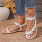 Woman's feet wearing white Korynn bohemian flat thong sandals adorned with delicate floral appliques and clear rhinestones, paired with blue denim jeans.