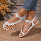 White Bohemian Korynn flat thong sandals adorned with delicate floral appliques and clear rhinestones, shown on a woman's feet with denim jeans and a gold anklet.