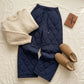 Kovara thermal quilted wide-leg trousers in midnight navy styled in a winter flat lay with a beige chunky knit sweater and shearling boots.