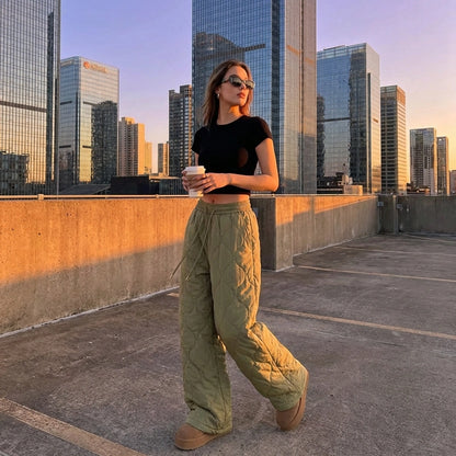Kovara thermal quilted wide-leg trousers in olive green, modeled on a city rooftop showing the diamond stitching and relaxed fit.