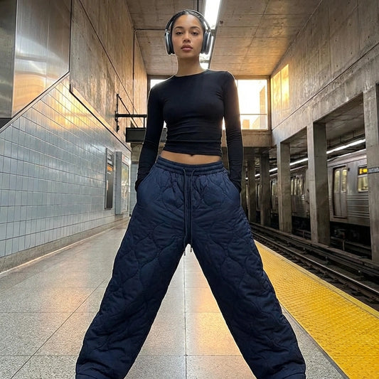 Kovara thermal quilted wide-leg trousers in navy blue, front view worn by a model in a subway station showing the diamond stitching and oversized fit.