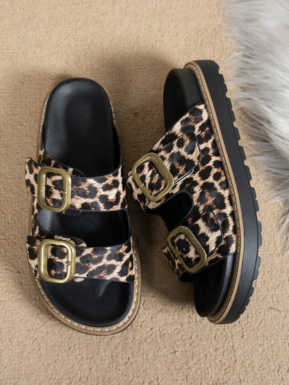 Kovari women's leopard print platform slide sandals with double antique gold buckles and a chunky black sole, shown at a three-quarter angle on a textured background.