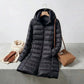 Kovera black long puffer coat with slim fit silhouette and removable hood, styled with a scarf, gloves, and handbag.