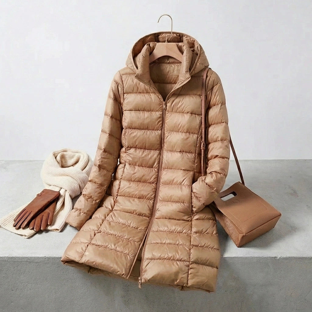 Kovera long puffer coat in khaki with removable hood, styled with a scarf, leather gloves, and a handbag on a studio background.