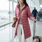 Kovera slim fit long puffer coat in soft rose pink worn by a woman in an airport terminal, showcasing the tailored silhouette and travel-ready style.