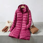 Kovera long puffer coat in deep magenta with slim fit silhouette and removable hood, styled with scarf, gloves, and handbag.