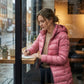 Kovera soft rose long puffer coat with slim fit and removable hood worn by a woman writing in a cafe on a rainy day.