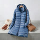 Kovera steel blue long puffer coat with removable hood, styled with a scarf, leather gloves, and a handbag on a concrete surface.