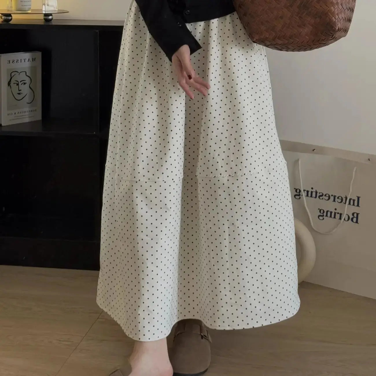 Kozira Soft Apricot polka dot A-line midi skirt on a model, highlighting its elegant flowing silhouette, midi-length, and distinctive architectural mid-seam detail in a lifestyle setting.