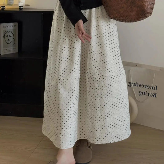 Kozira Soft Apricot polka dot A-line midi skirt on a model, highlighting its elegant flowing silhouette, midi-length, and distinctive architectural mid-seam detail in a lifestyle setting.